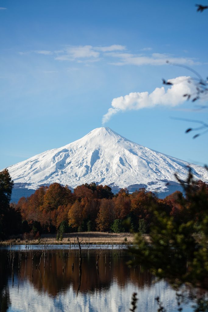Vista majestuosa del Volcán Villarrica con follaje de otoño y reflejos en el lago.